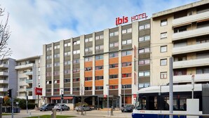 Un hotel de varios pisos con un llamativo letrero 'ibis HOTEL', una parada de autobús y un aparcamiento con coches.