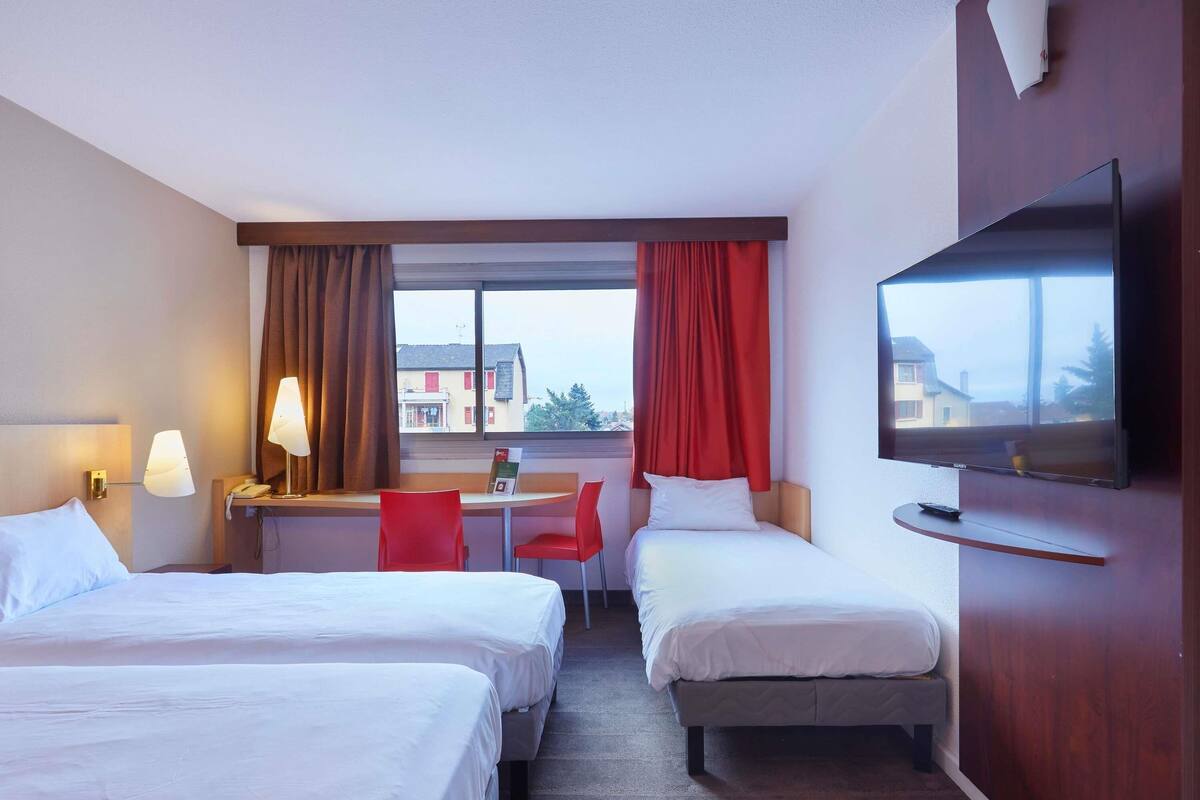 A hotel room with two beds, a desk, a chair, a television, and a window with curtains.