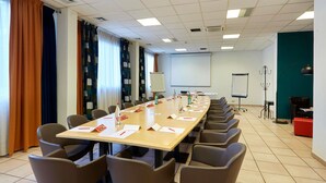 Una sala de conferencias con una larga mesa, sillas, una pantalla de proyector y una pizarra.