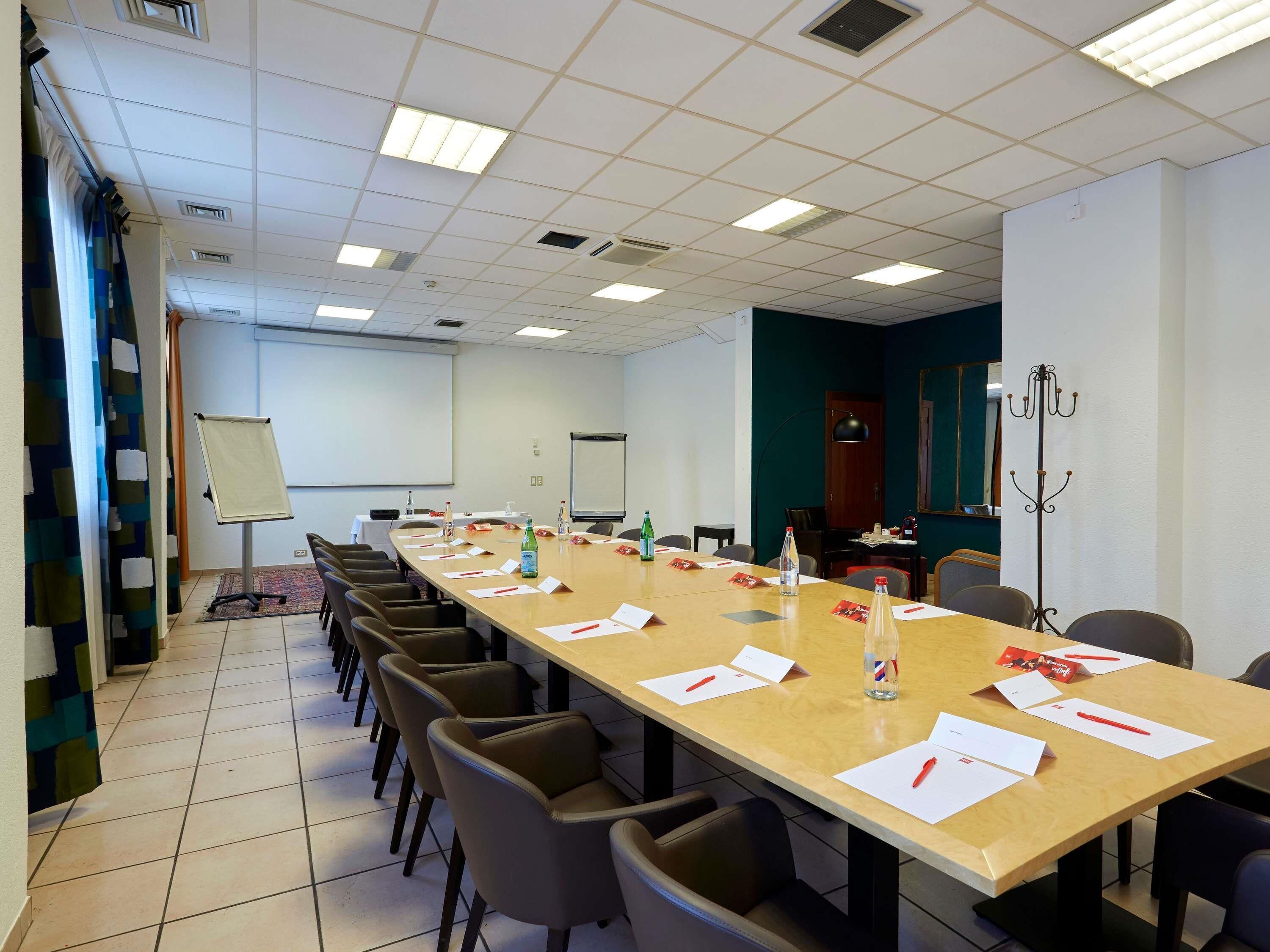 Une salle de conférence équipée d’une longue table, de chaises, d’un écran de projection et d’un tableau blanc.