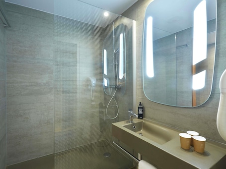 A modern bathroom with a glass shower enclosure, a beige sink with a mirror, and a towel rack.. ibis Annemasse