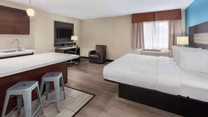 A hotel room with a large bed, a desk with a chair, a small kitchenette, and a TV.