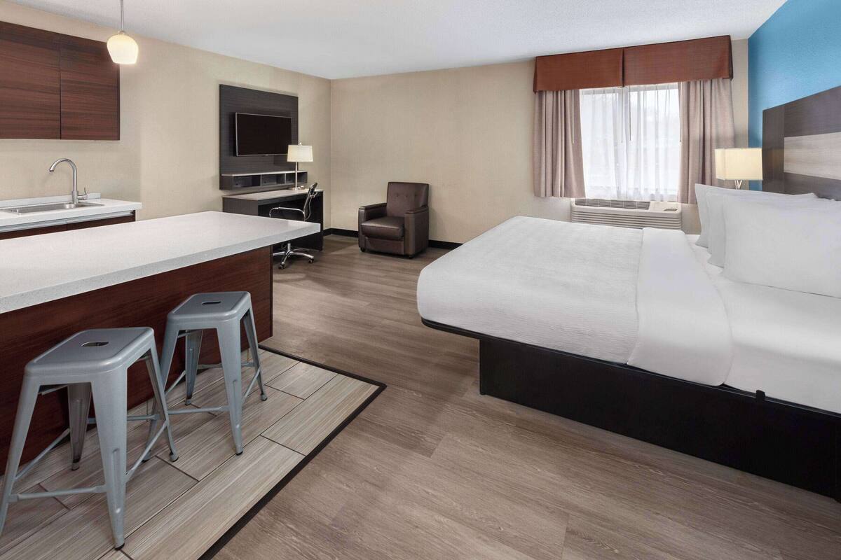 A hotel room with a large bed, a desk with a chair, a small kitchenette, and a TV.
