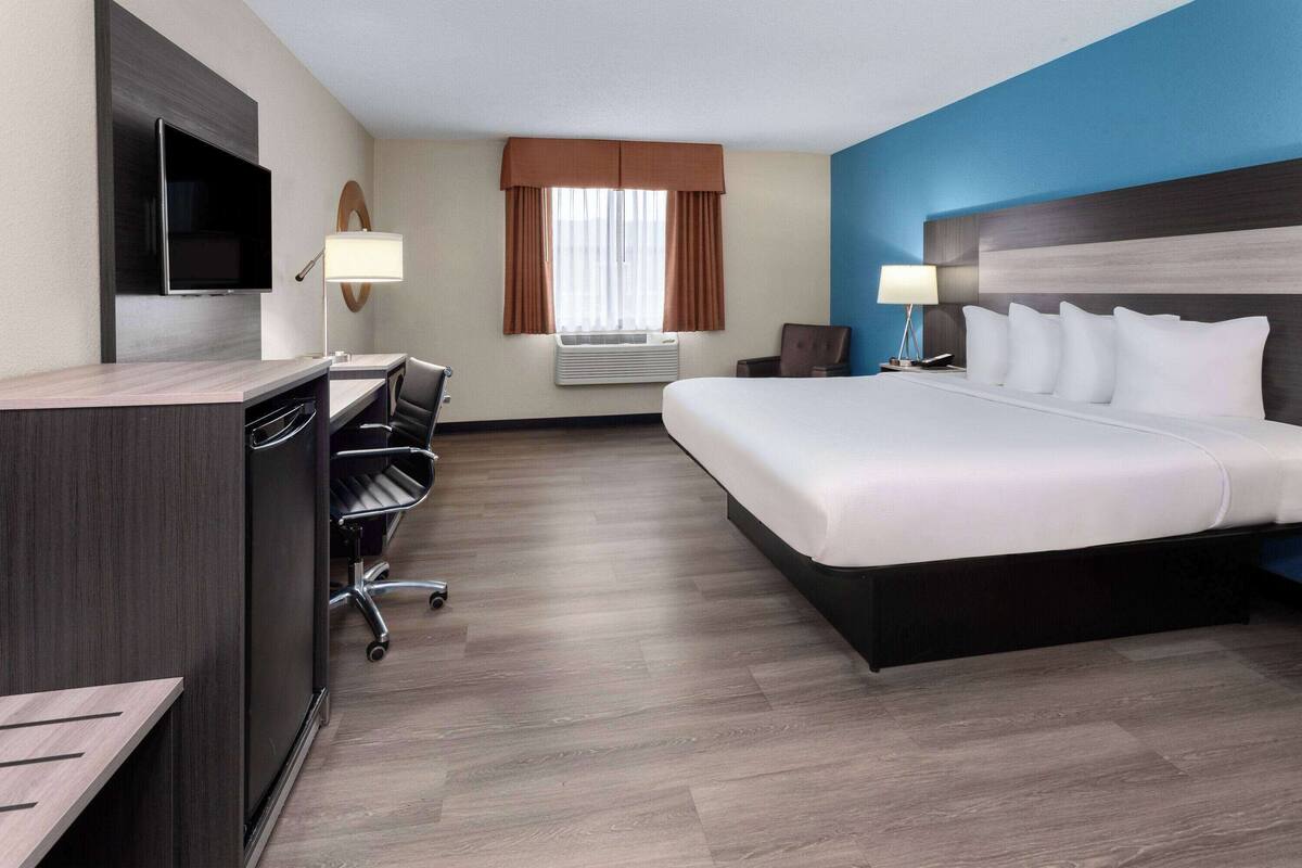 A hotel room with a large bed, a desk with a chair, a television, and a window with curtains.