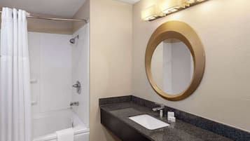 A bathroom with a bathtub, a sink with a mirror, and a shower curtain.