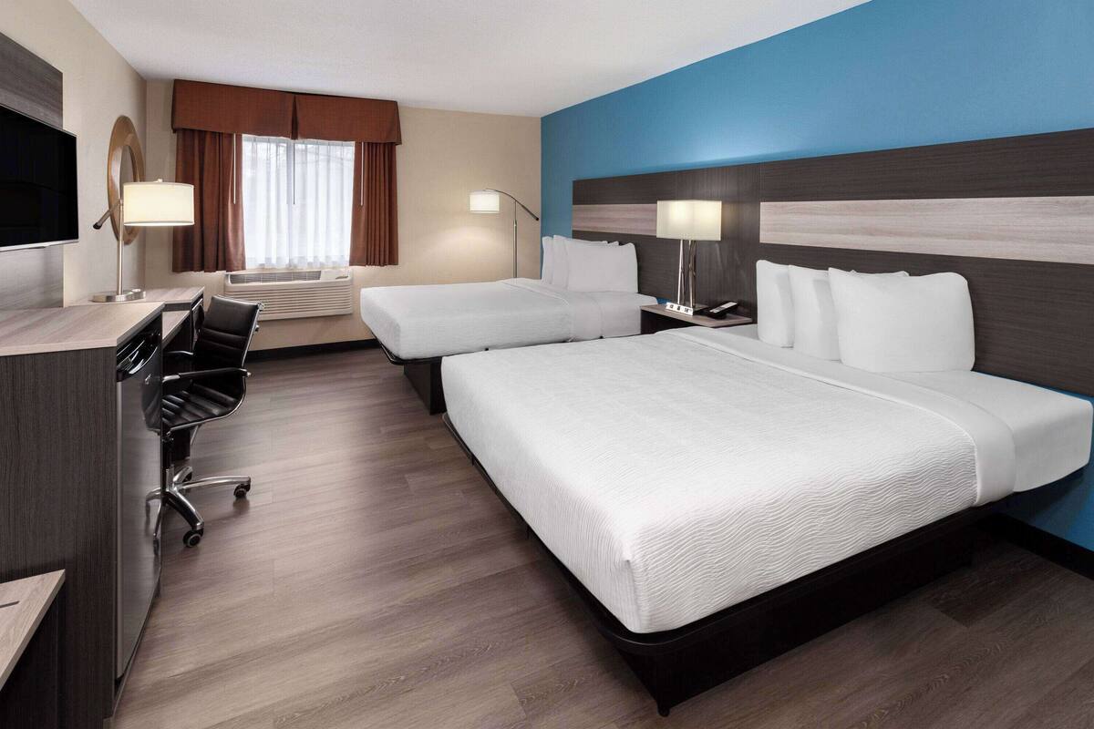 A hotel room with two beds, a desk, a chair, a TV, and a window with curtains.