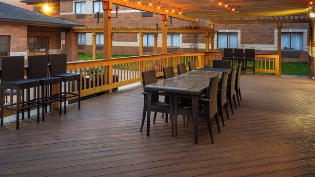 An outdoor deck with a wooden railing, a glass-top table, and multiple chairs.