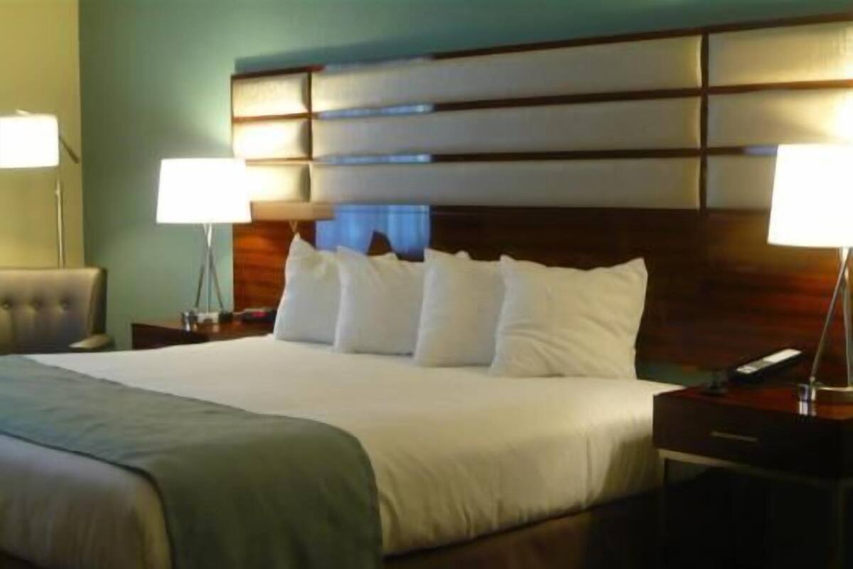 A hotel room with a large bed, two bedside tables, a nightstand, and a lamp.