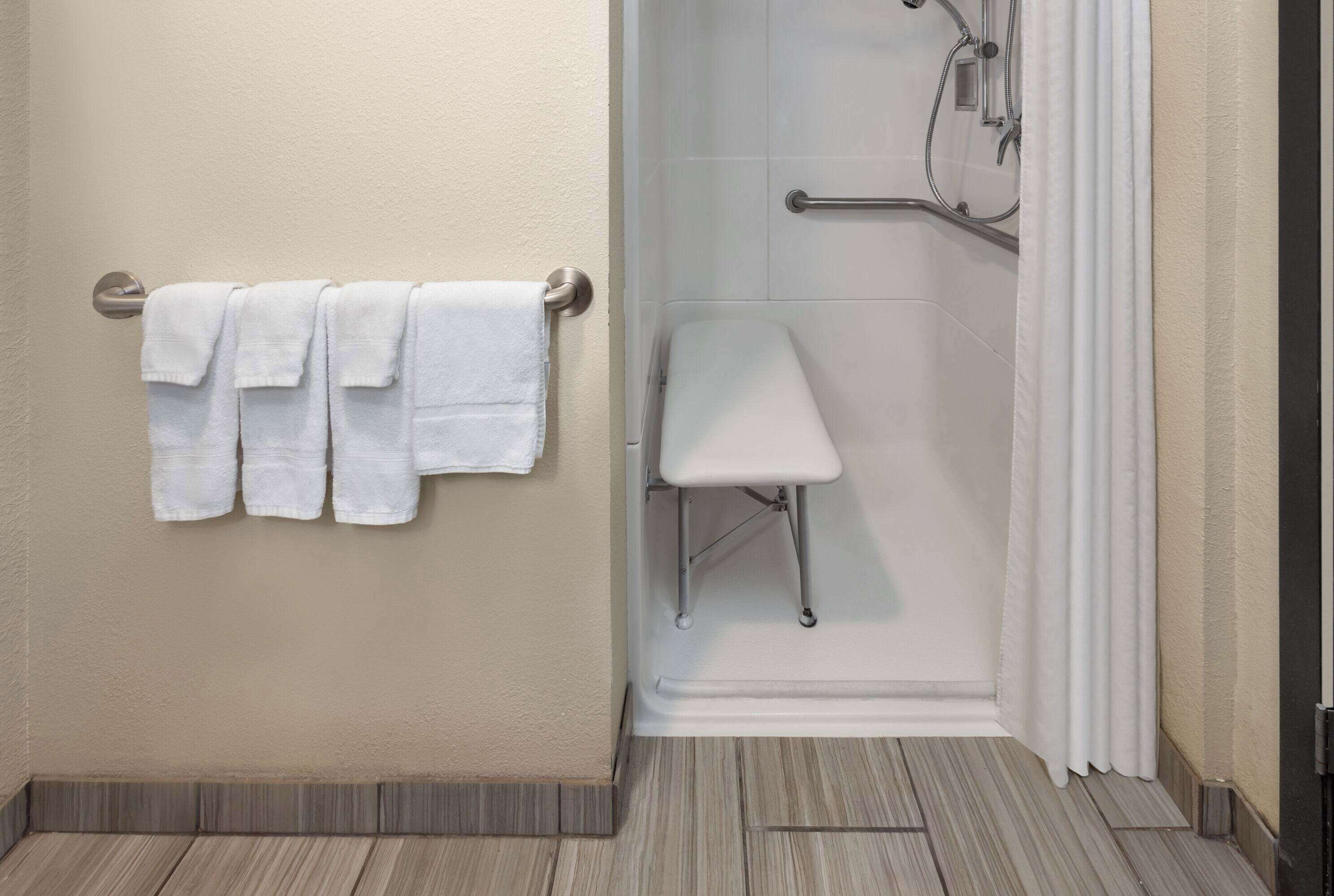 A bathroom with a shower, a white towel rack, and a white bench.