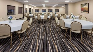 A conference room with multiple round tables, each with chairs, and a carpeted floor.
