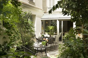 An outdoor patio with a table and chairs, surrounded by various potted plants and greenery. - Hôtel A La Villa des Artistes (Paris)