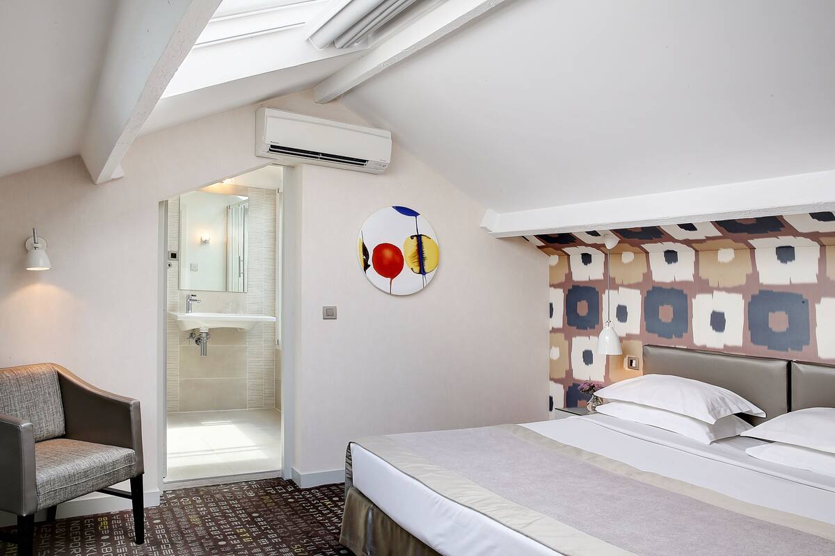 Una habitación de hotel con tragaluz, ducha, cama con ropa blanca y pared con diseño.