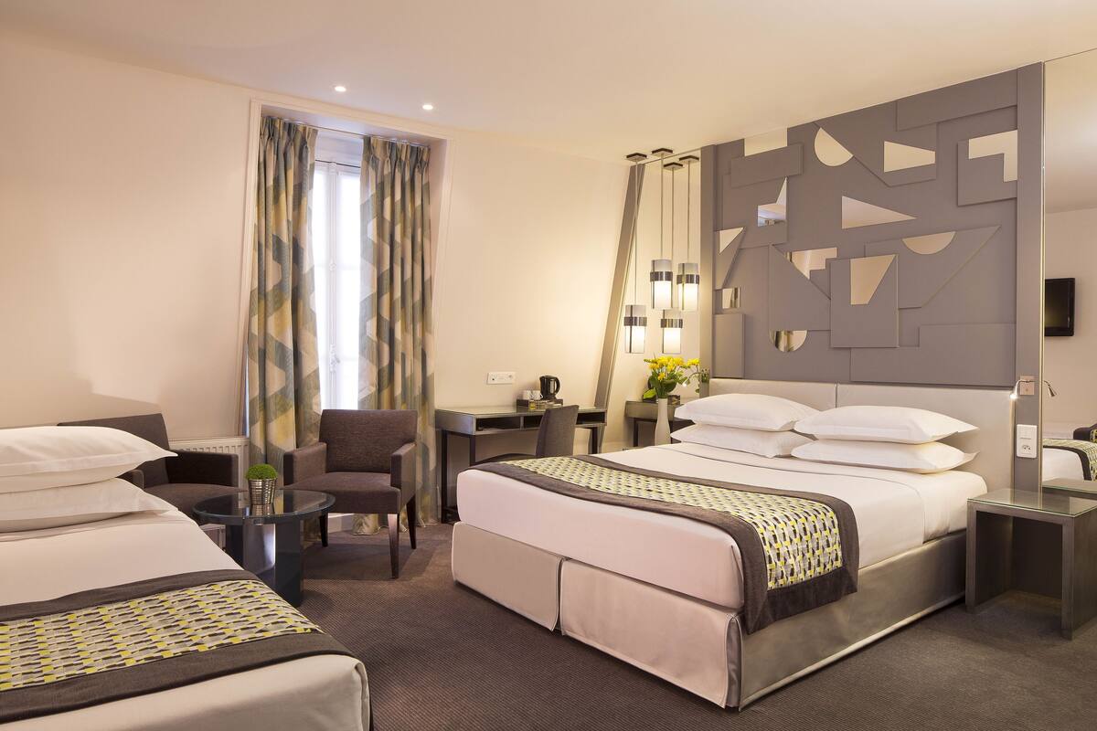 Habitación de hotel con dos camas, un escritorio, una silla y una mesita.