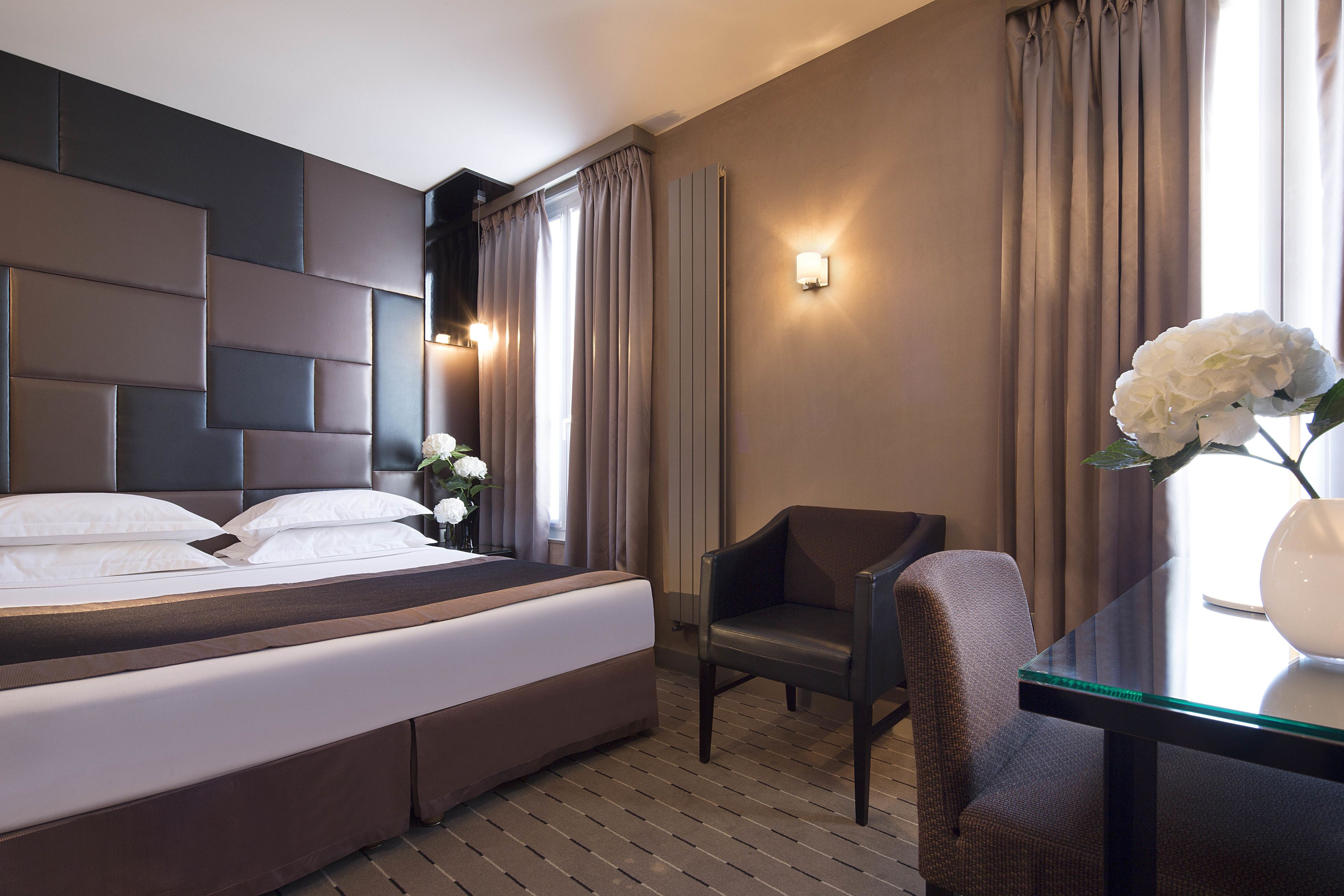A hotel room with a large bed, a chair, a table, and a vase with flowers.