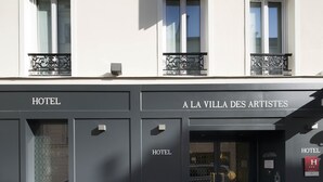 Fachada de hotel con balcones, un letrero que dice "A LA VILLA DES ARTISTES" y varios letreros que indican "HOTEL".