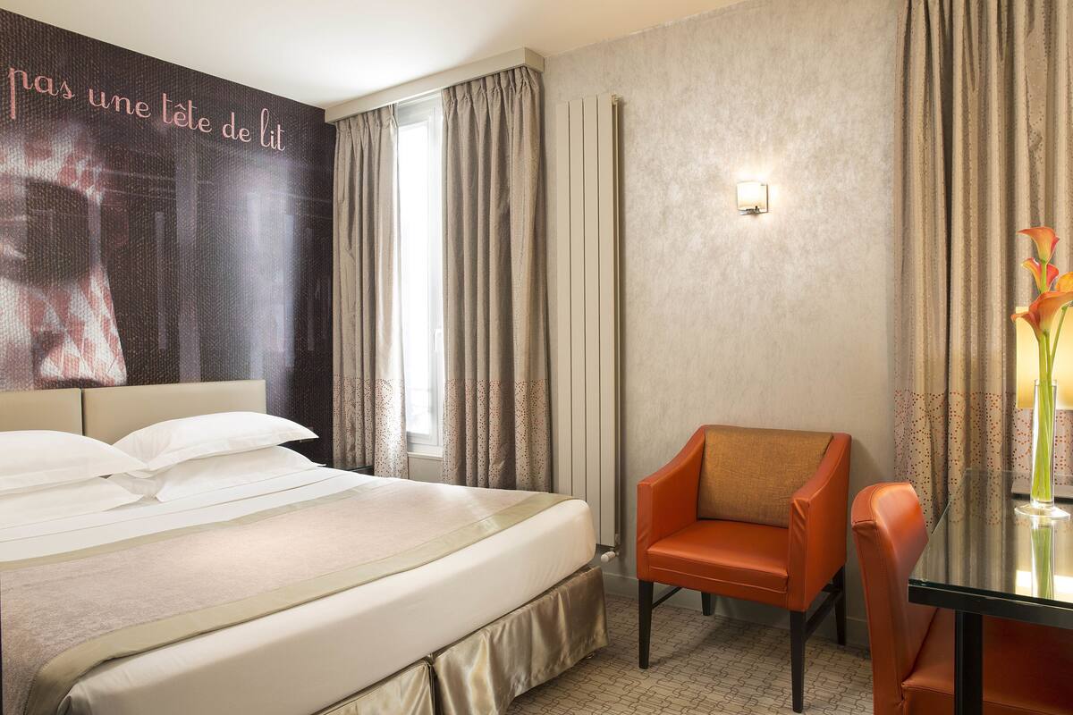 Una habitación de hotel con cama, una silla, una mesa y un cartel en la pared.