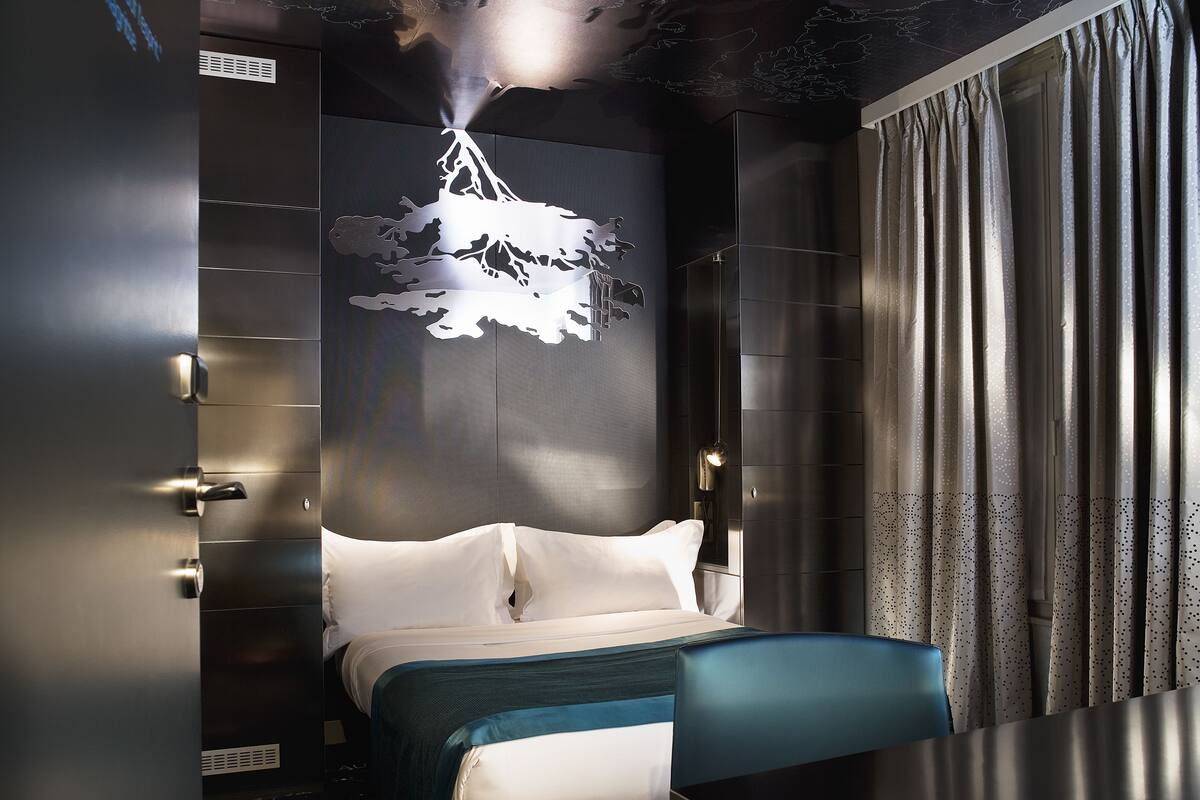 Una habitación de hotel moderna con una cama, un aplique de pared y una cortina.