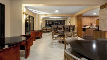 Un comedor moderno con varias mesas y sillas, una cocina al fondo y vistas de la ciudad de noche.
