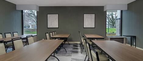 Un salón de conferencias con mesas largas y sillas, ventanas amplias y obras de arte en las paredes.