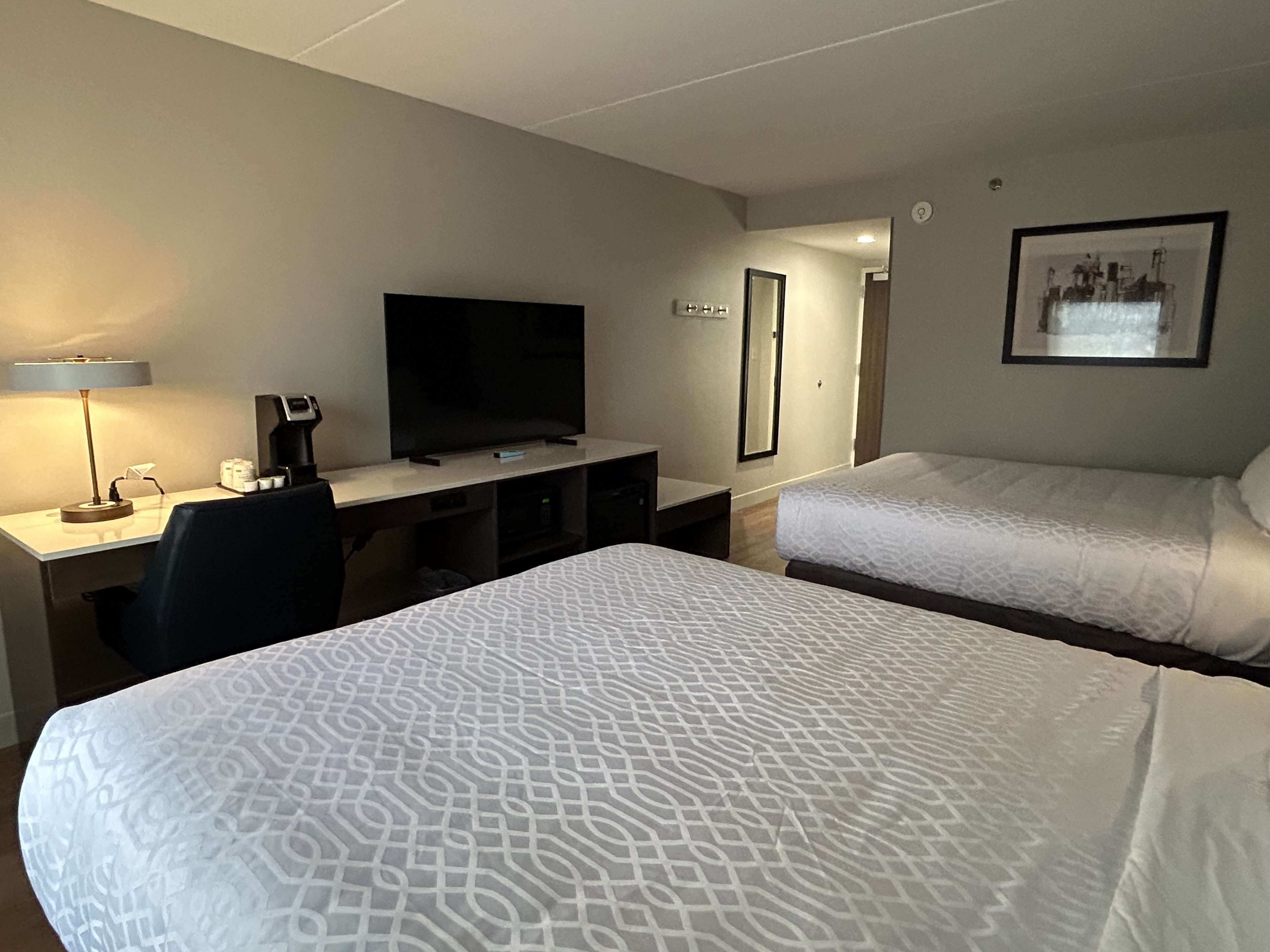 Una habitación de hotel con dos camas, un escritorio, un televisor, una cafetera y un espejo.