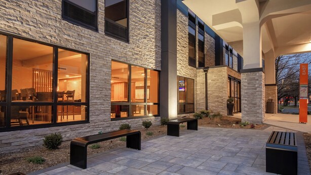 Un edificio moderno con grandes ventanales, asientos al aire libre y fachada de piedra.