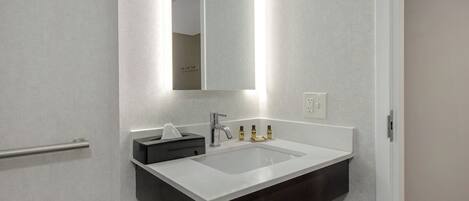 Un baño moderno con lavamanos blanco, tocador oscuro y espejo con iluminación integrada.