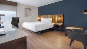 Una habitación de hotel moderna con cama, escritorio, silla y mesita de noche con lámpara.