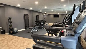 Un gimnasio con cintas de correr, mancuernas y pelotas de ejercicio.