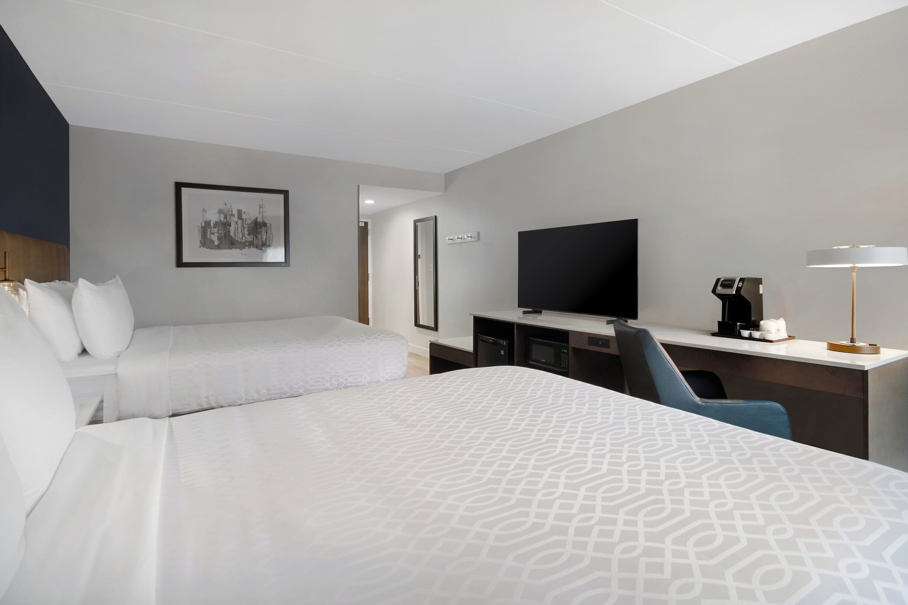 A hotel room with two beds, a desk with a television, a coffee maker, and a lamp.