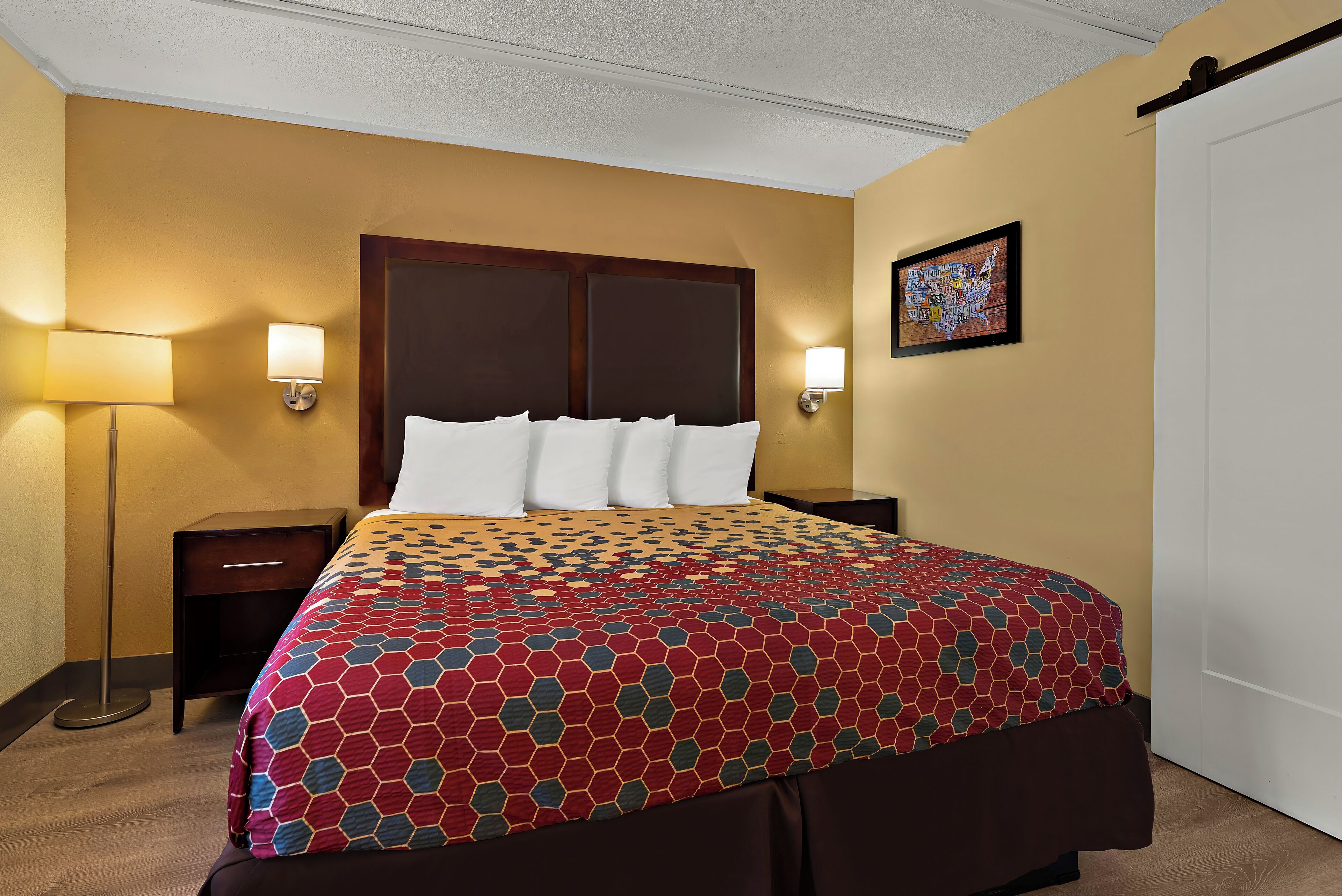 A hotel room with a large bed, two bedside tables, a floor lamp, and a wall map.