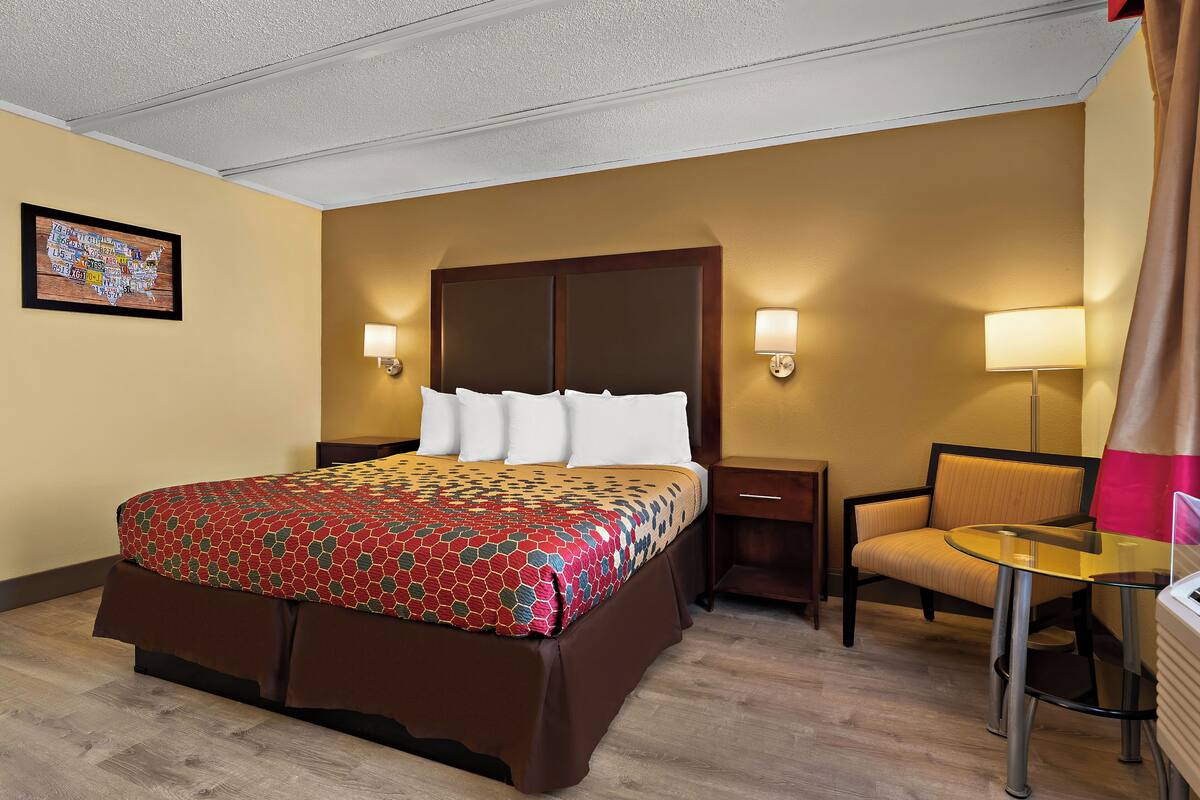 A hotel room with a large bed, two bedside tables, a chair, and a small table.