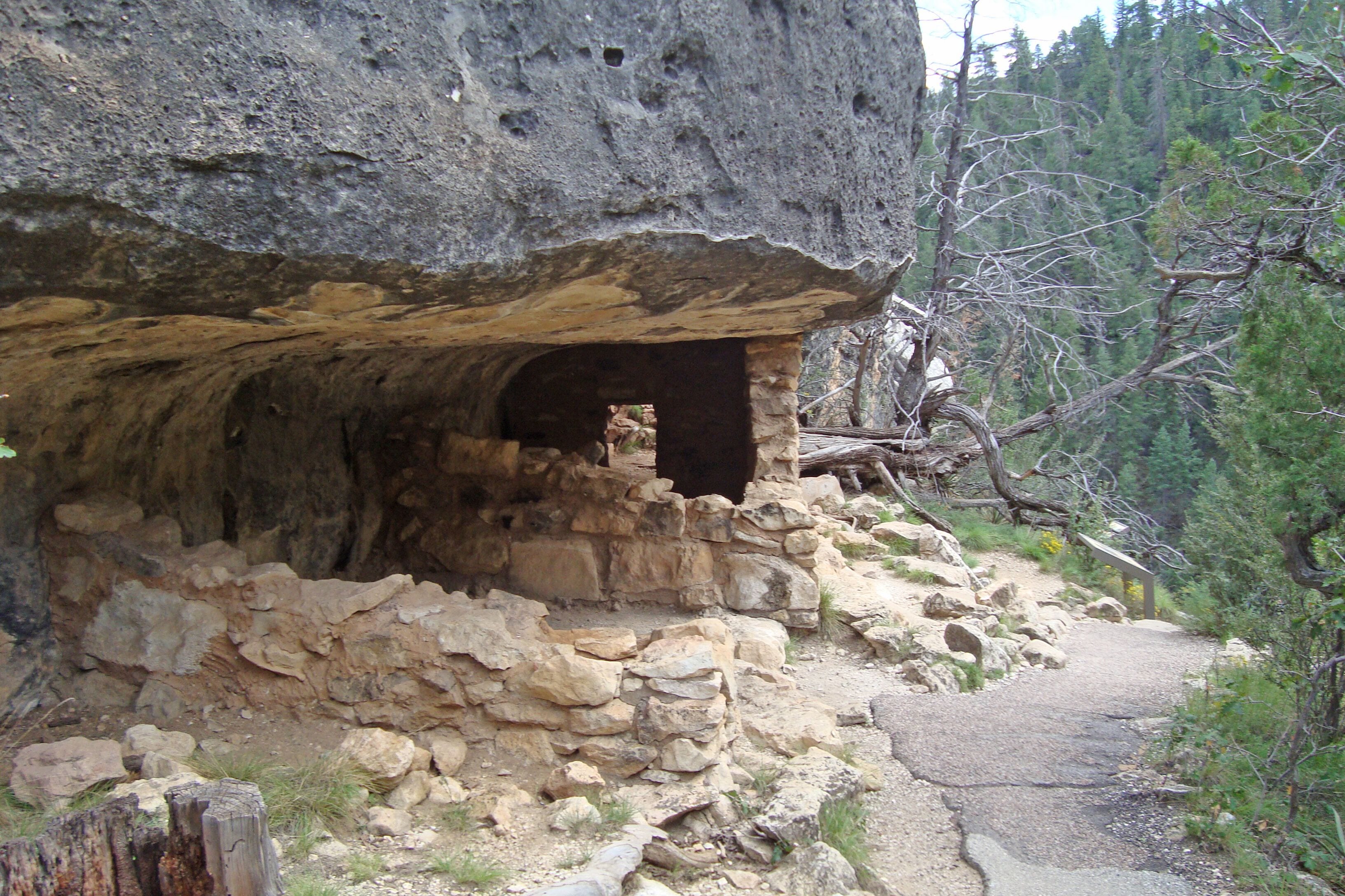 L’entrée d’une grotte, avec une structure en pierre et un sentier menant à la forêt.