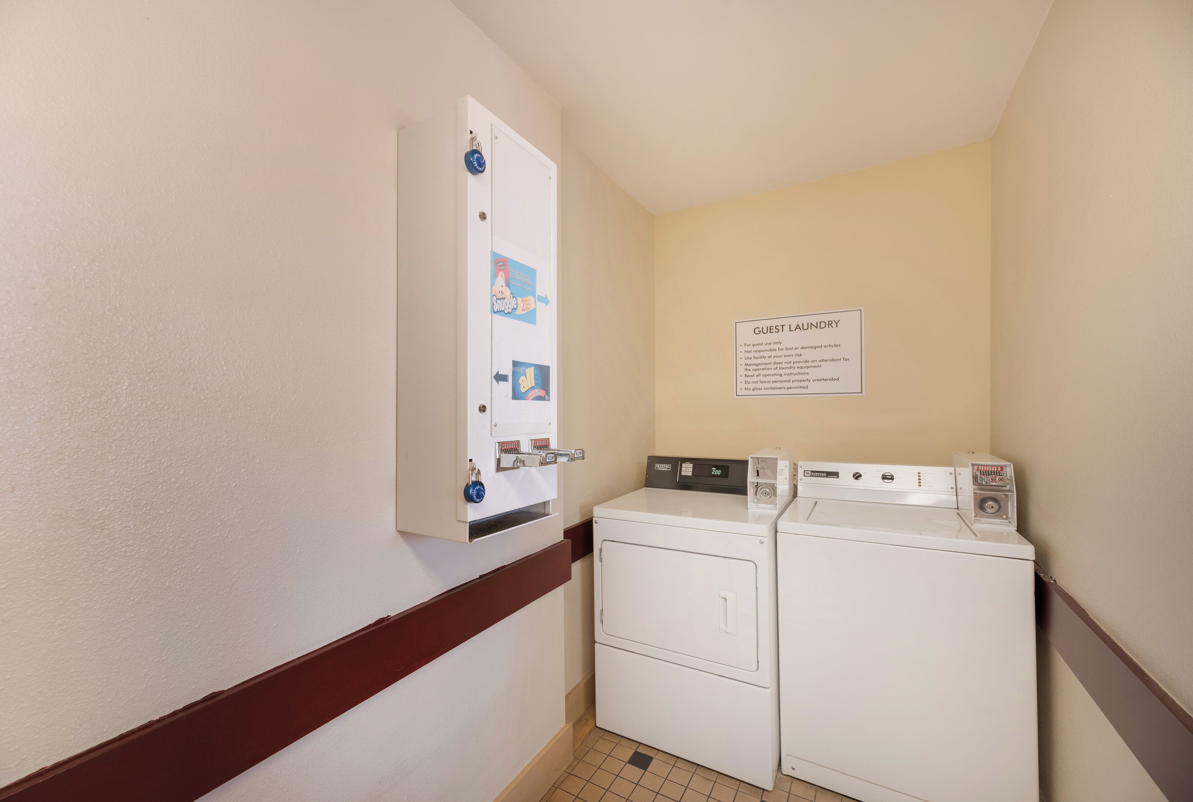 Una sala de bugaderia amb una rentadora i una assecadora muntades a la paret, i un cartell amb les normes de la bugaderia per a hostes.