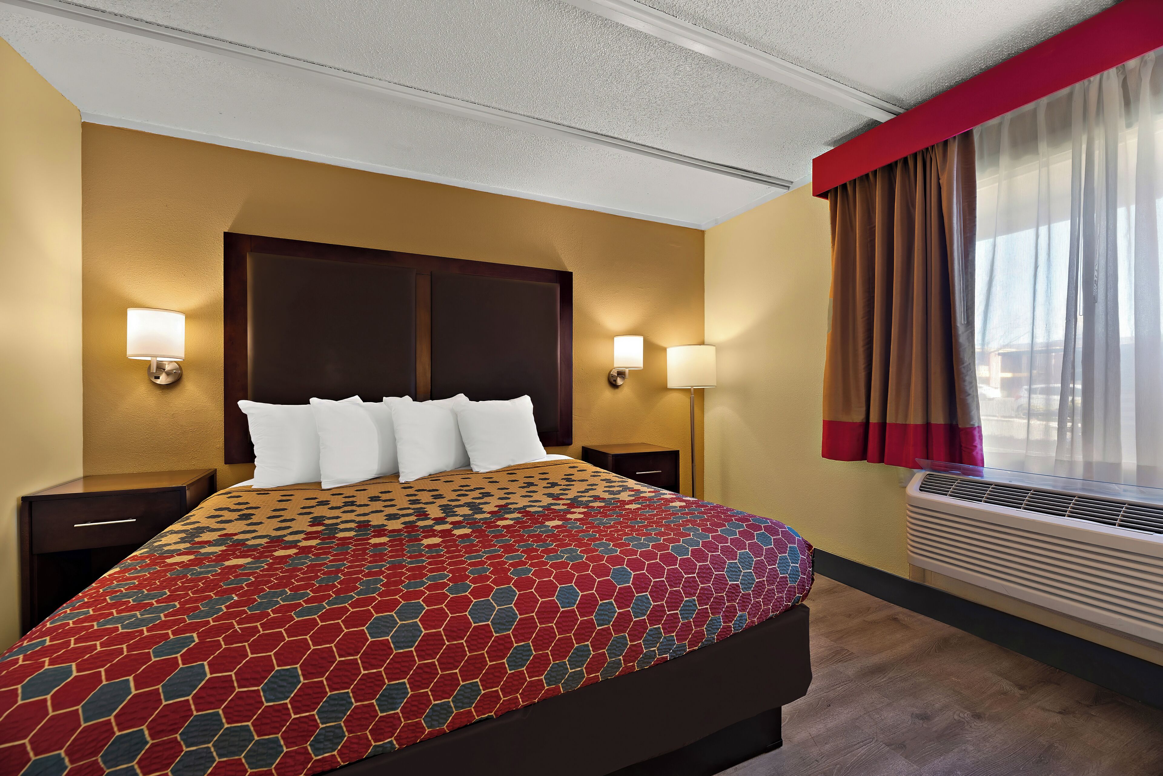 Une chambre d’hôtel avec un grand lit, deux tables de chevet, une fenêtre avec des rideaux et un appareil de climatisation.