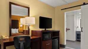 A hotel room with a wooden desk, a television, a microwave, a refrigerator, a telephone, and a mirror. - Kings House Motor Hotel, a Dazzler Select by Wyndham (Flagstaff)