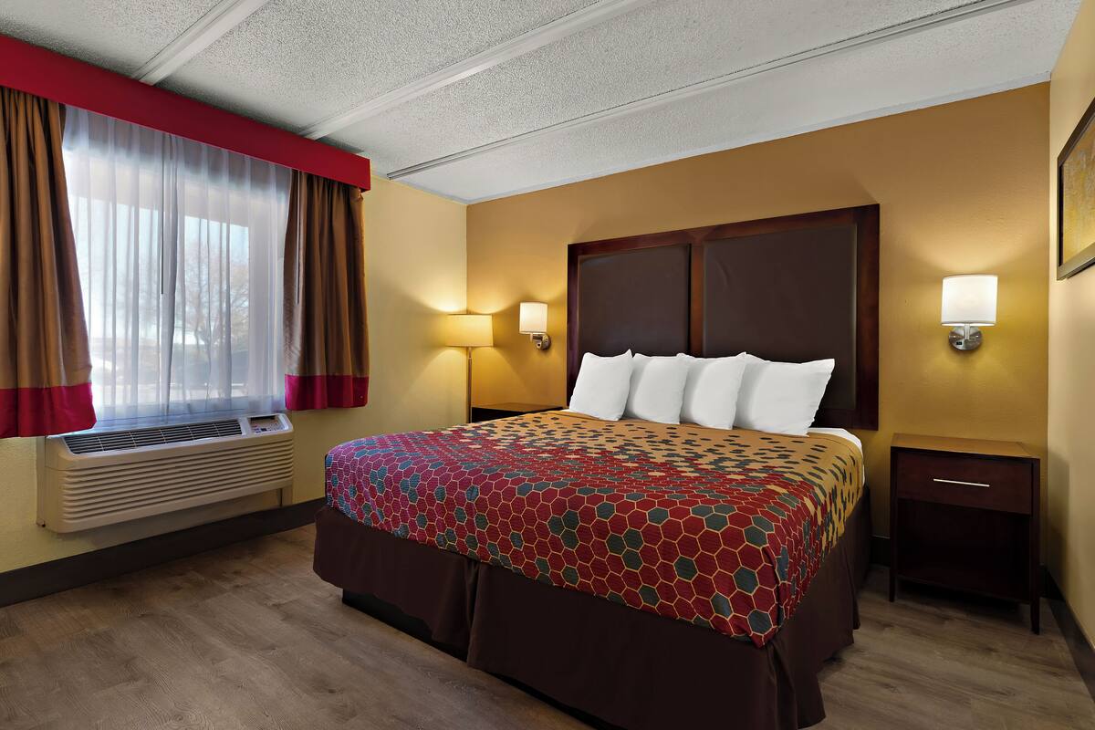 A hotel room with a large bed, a bedside table, a lamp, and a window with curtains.