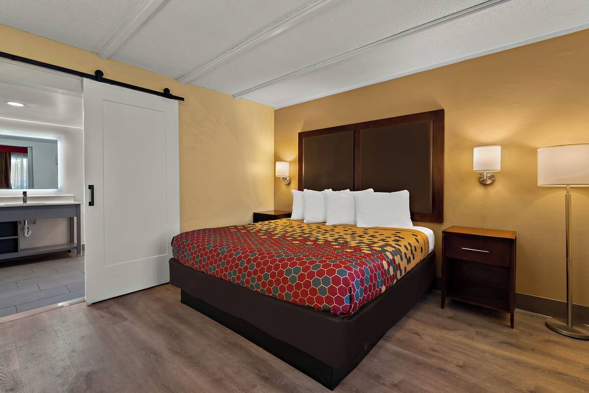 A hotel room with a bed, bedside tables, a mirror, and a sliding door.