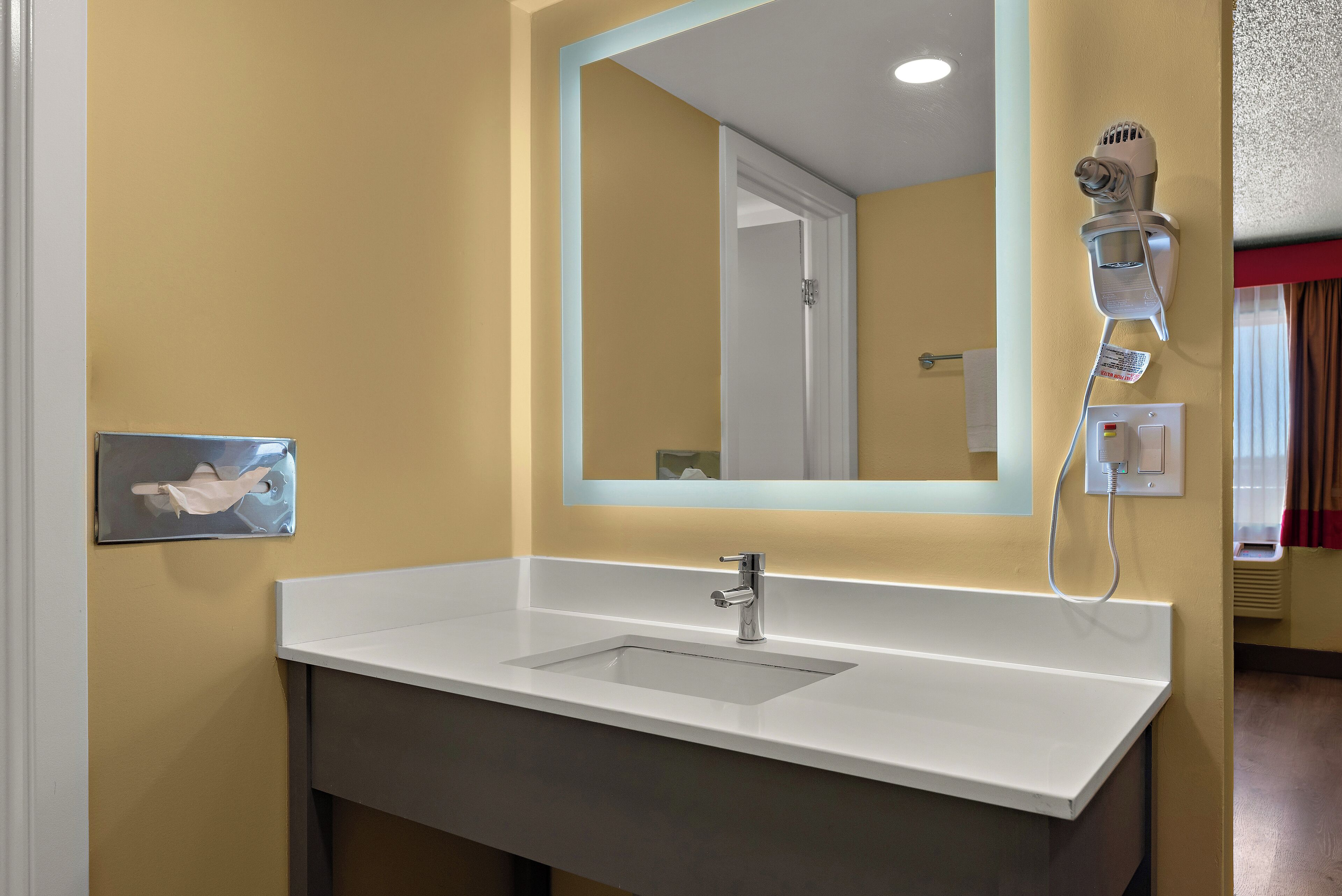 Une salle de bain avec un lavabo blanc, un miroir et un sèche-cheveux fixé au mur.
