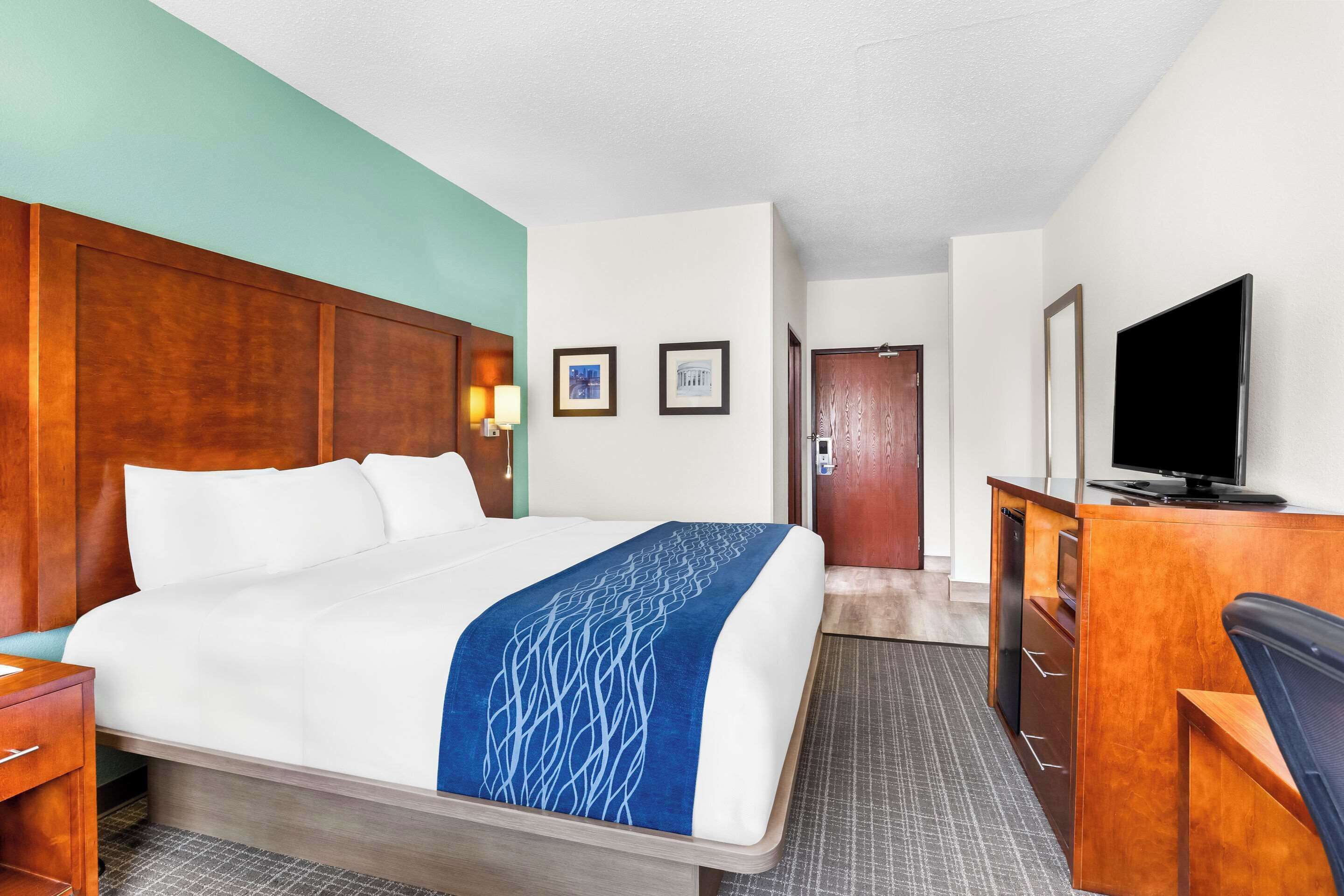 A hotel room with a large bed, a desk with a television, and a door leading to another room.