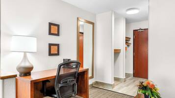 Habitación de hotel con un escritorio de madera, una silla, una lámpara, un espejo y un florero con flores.