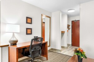 Habitación de hotel con un escritorio de madera, una silla, una lámpara, un espejo y un florero con flores.