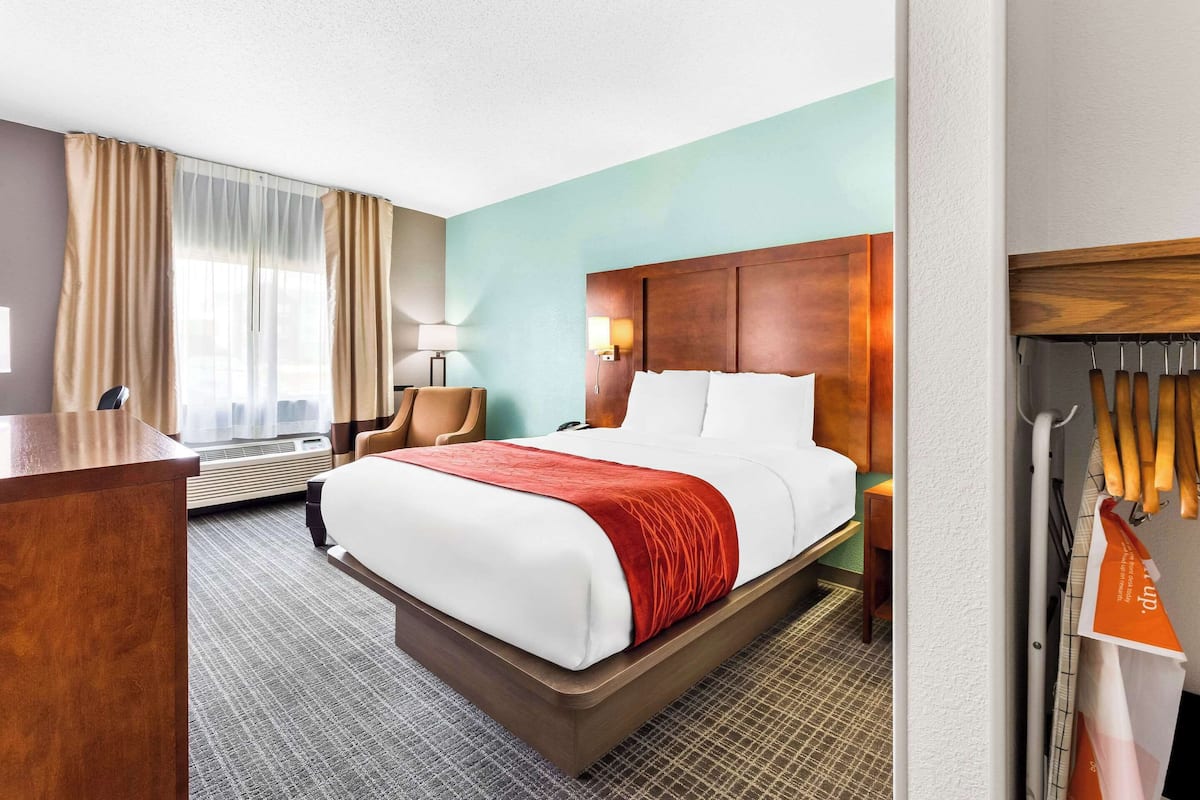 A hotel room with a large bed, a desk, a chair, a wardrobe, and a window with curtains.