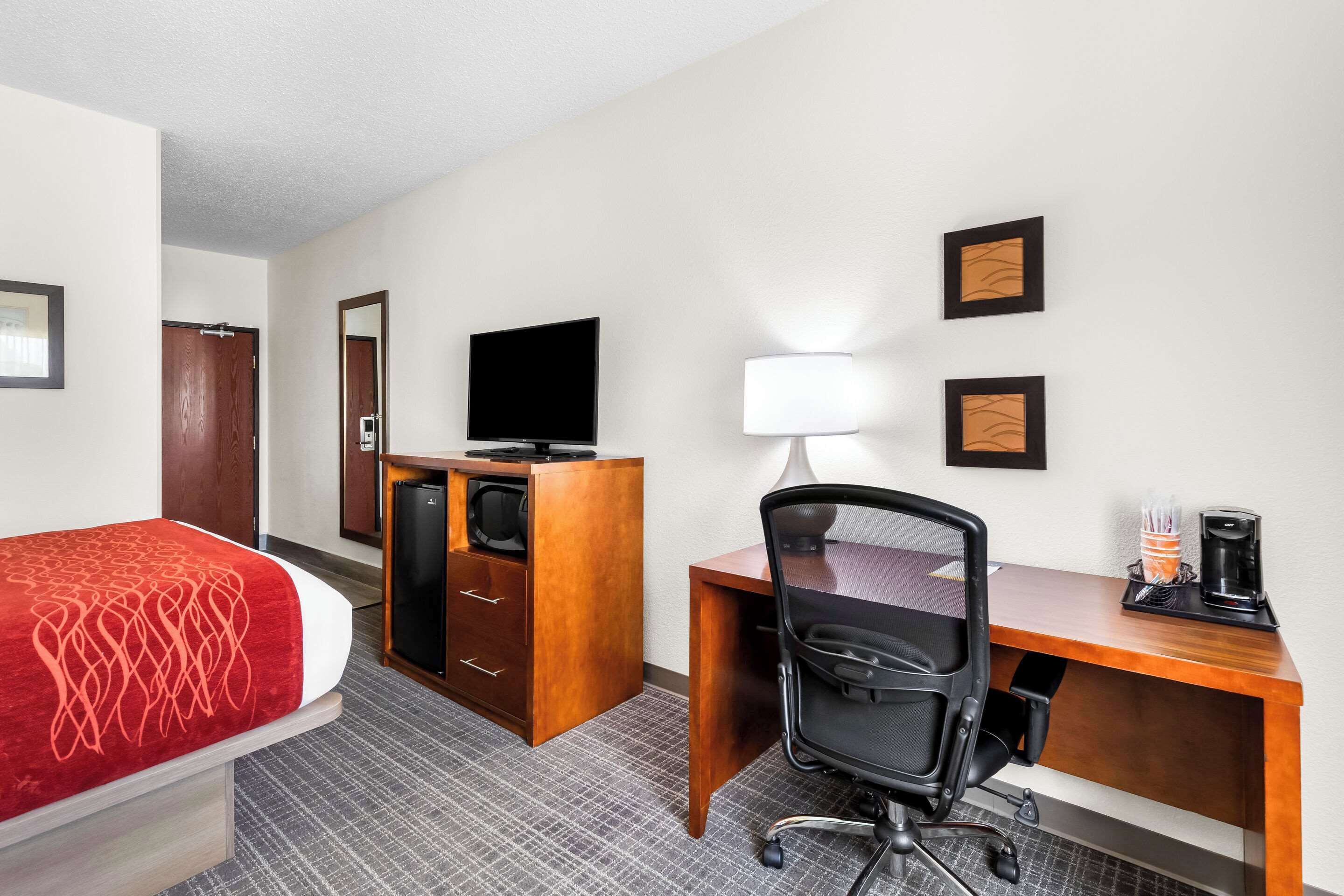 A hotel room with a bed, a desk, a chair, a television, a lamp, and a coffee maker.