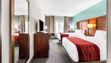 Habitación de hotel con una cama grande, una cama más pequeña, un escritorio, un televisor y un espejo.