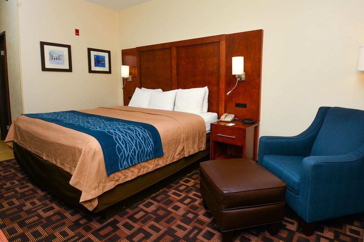 A hotel room with a bed, bedside table, chair, and a patterned carpet.