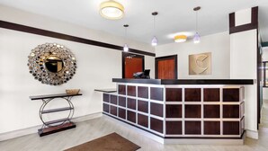 A reception area with a modern design, including a reception desk, a decorative mirror, and a wooden floor.
