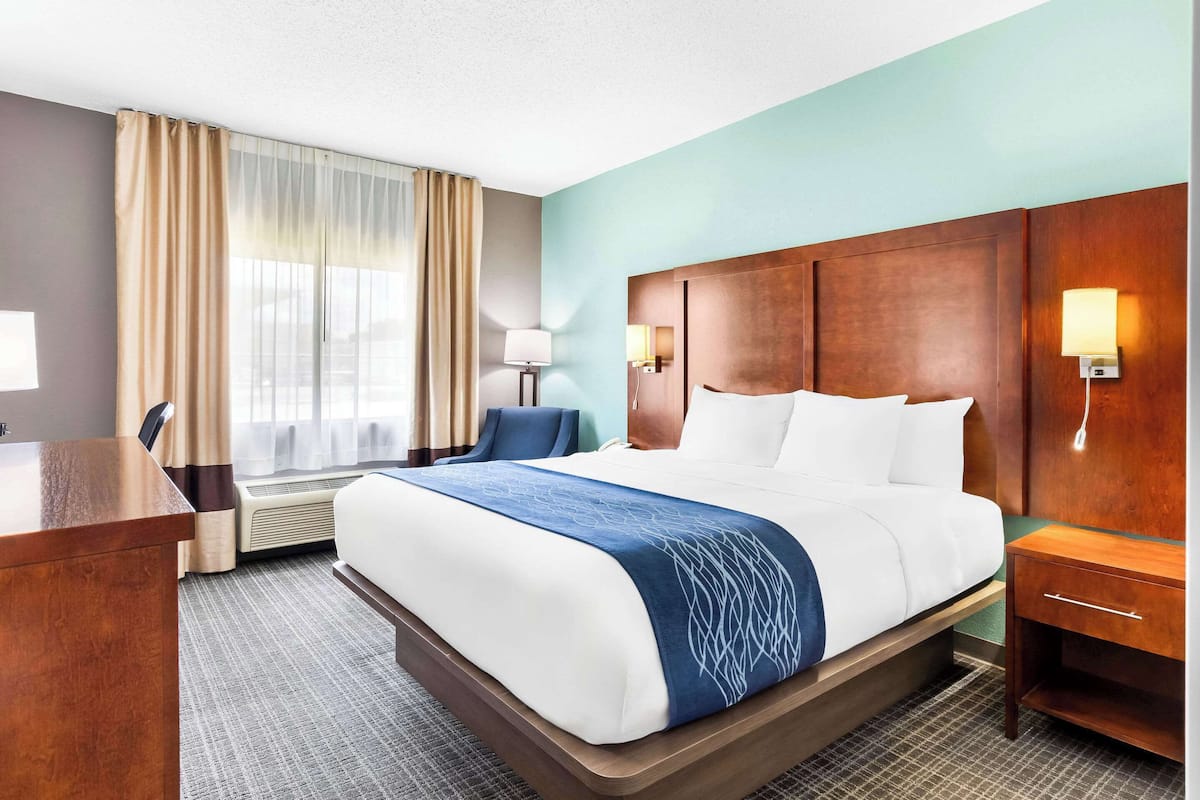 A hotel room with a large bed, a desk, a chair, a lamp, and a window with curtains.