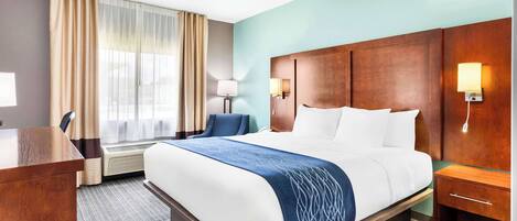 A hotel room with a large bed, a desk, a chair, a lamp, and a window with curtains.