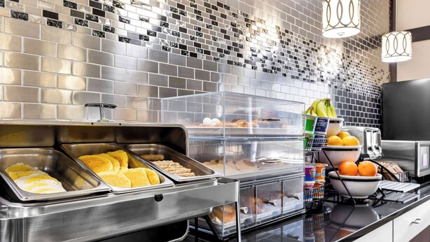 A buffet area with various food items in trays, a microwave, and a beverage dispenser.