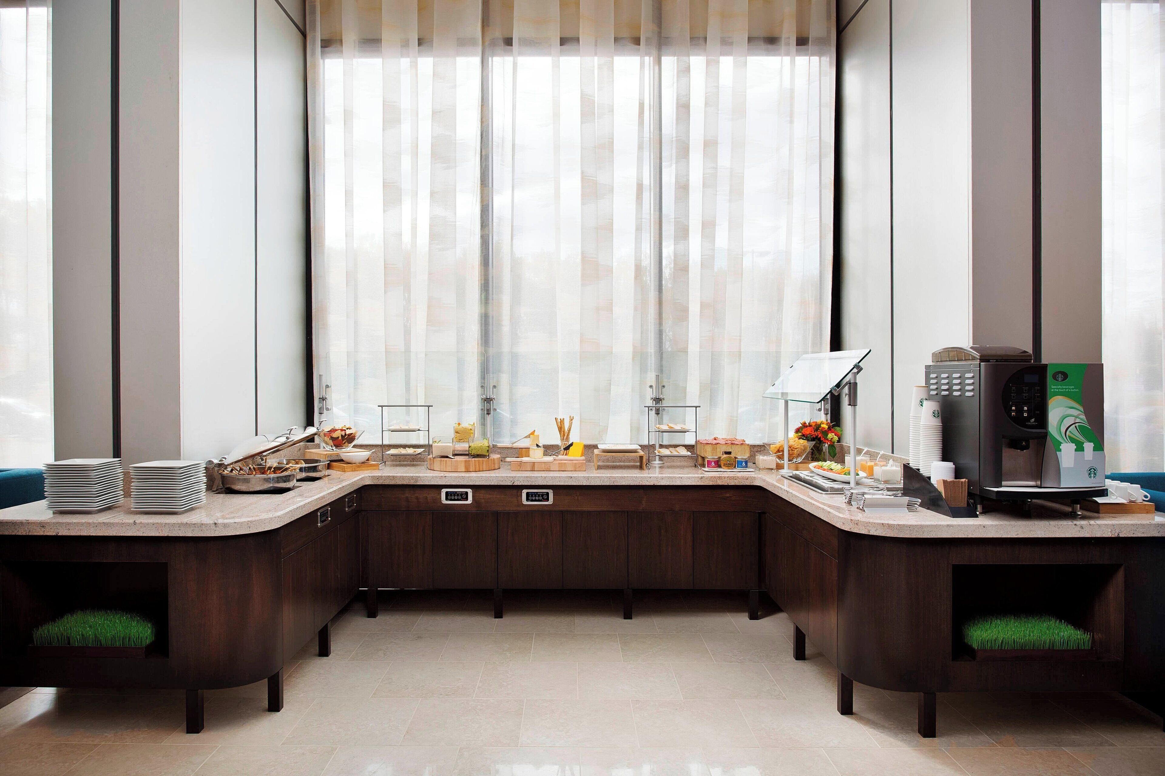 Un área de cocina moderna con cafetera, mesas de buffet y vistas amplias a través de grandes ventanales.